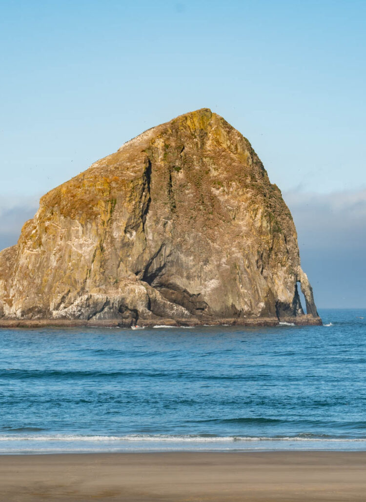 Haystack Rock at Cape Kiwanda in Pacific City, Oregon, with two people walking the beach